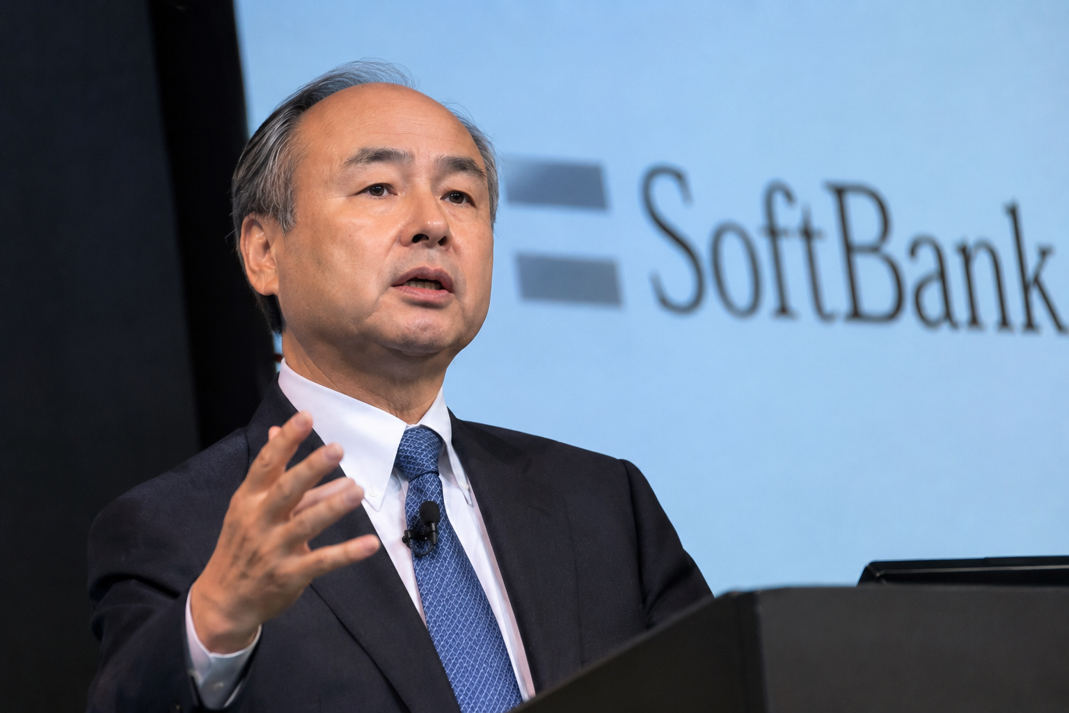Masayoshi Son speaking at a SoftBank event with the SoftBank logo in the background