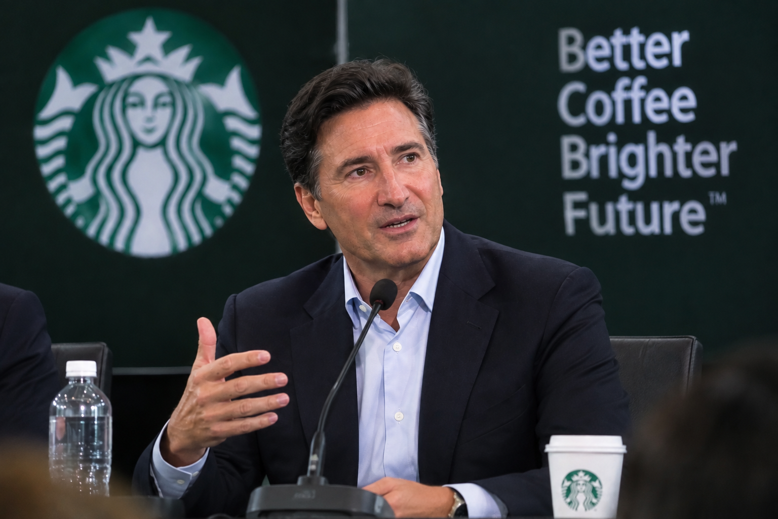 Brian Niccol, Starbucks chairman and CEO, speaking at a company event beside a "Better Coffee, Brighter Future" banner